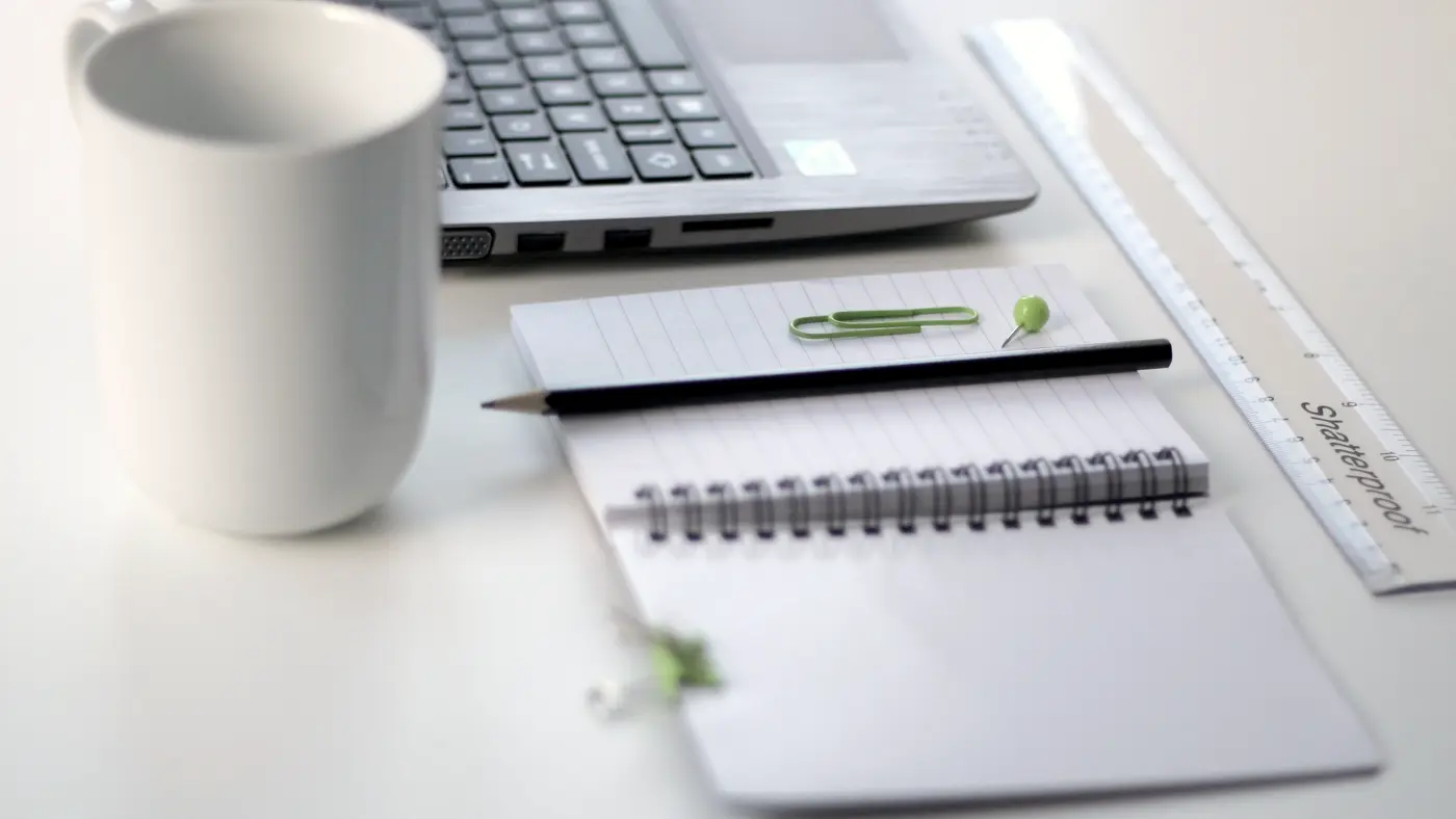 Notebook, pencil, coffee mug and laptop on a white desk