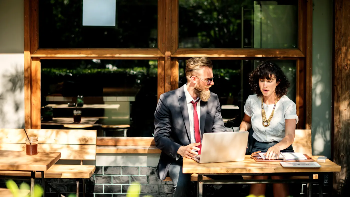 Two colleagues discussing work over a laptop at a wooden table