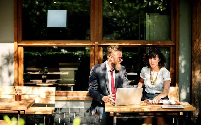 Two colleagues discussing work over a laptop at a wooden table