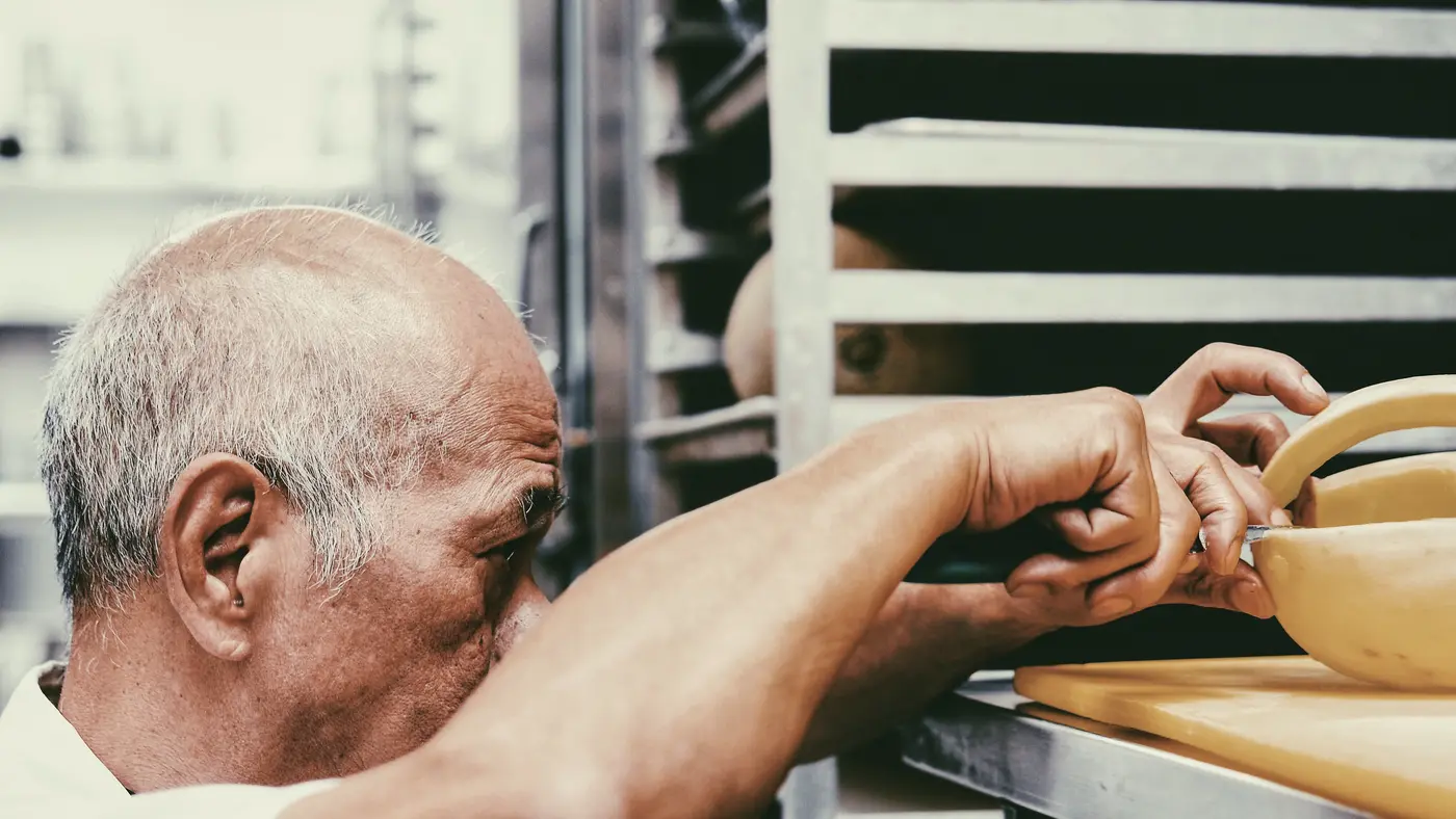 Older man working with trays at a bakery bench
