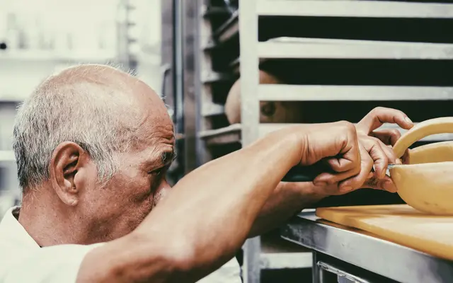 Older man working with trays at a bakery bench