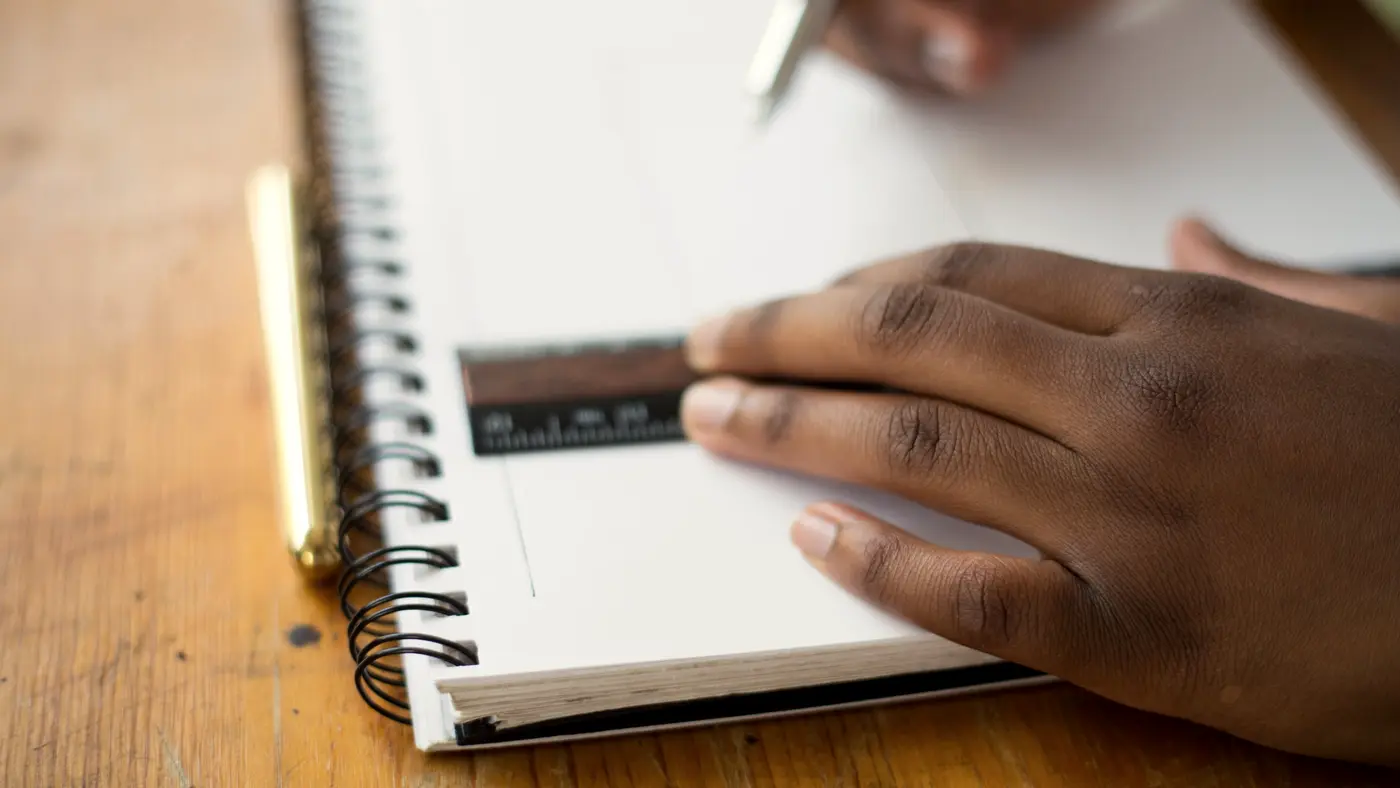 Hand writing in a spiral notebook on a wooden desk