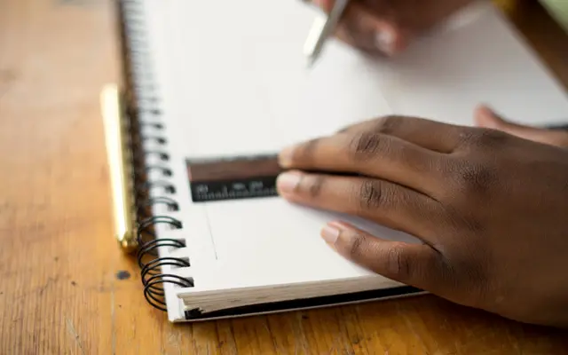 Hand writing in a spiral notebook on a wooden desk
