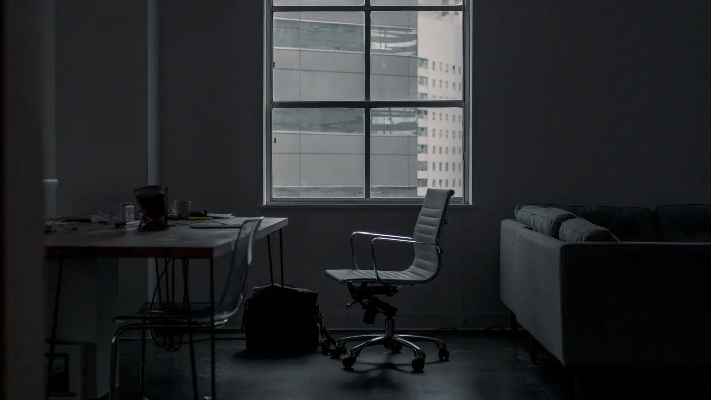 Dim loft office with a desk and chair beside tall windows