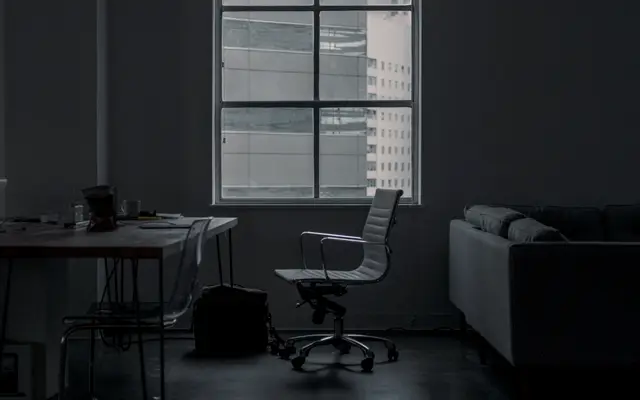 Dim loft office with a desk and chair beside tall windows