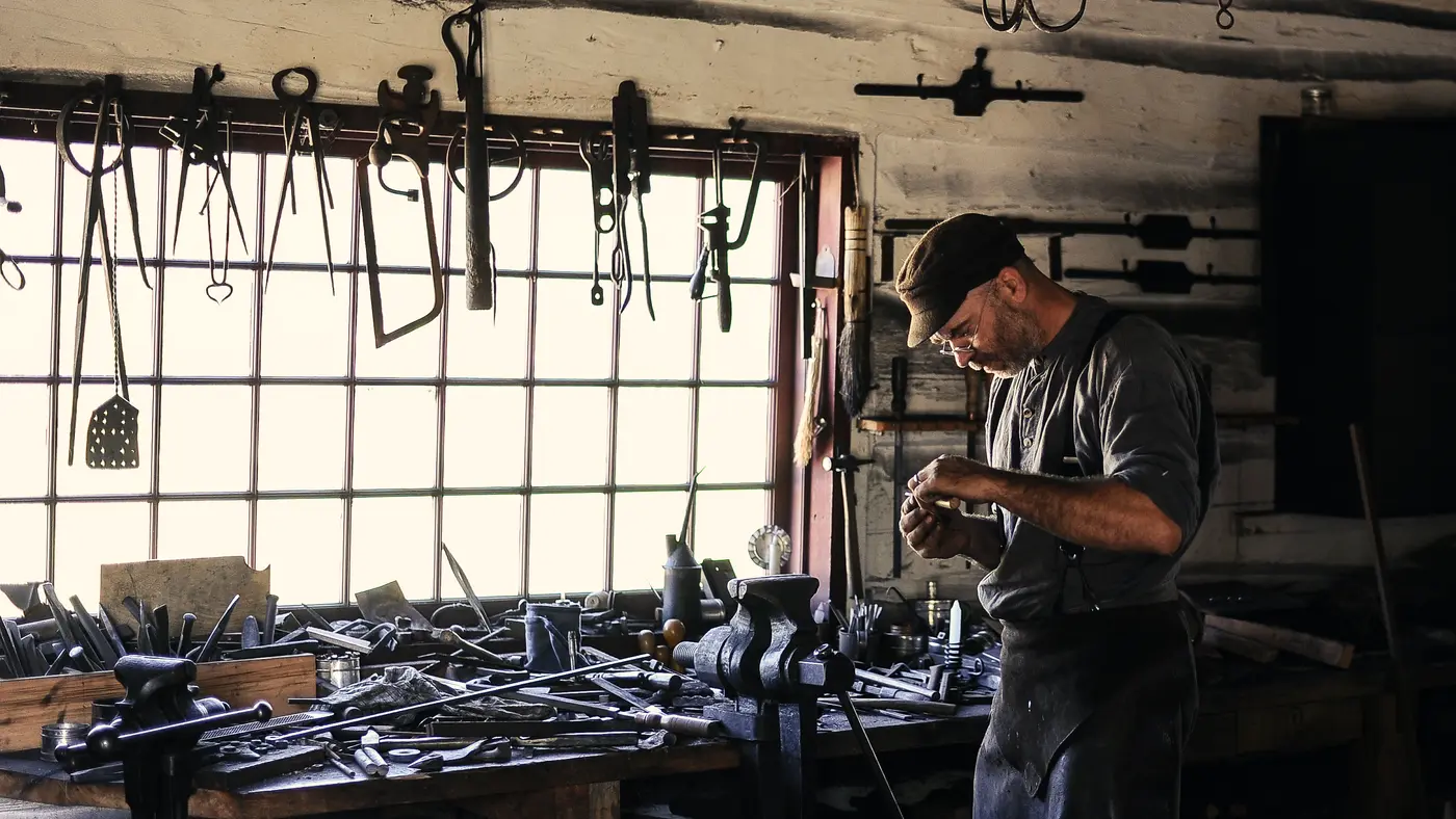 Metalworker at a bench in a workshop lined with hanging tools