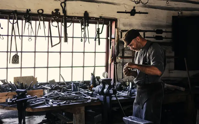 Metalworker at a bench in a workshop lined with hanging tools