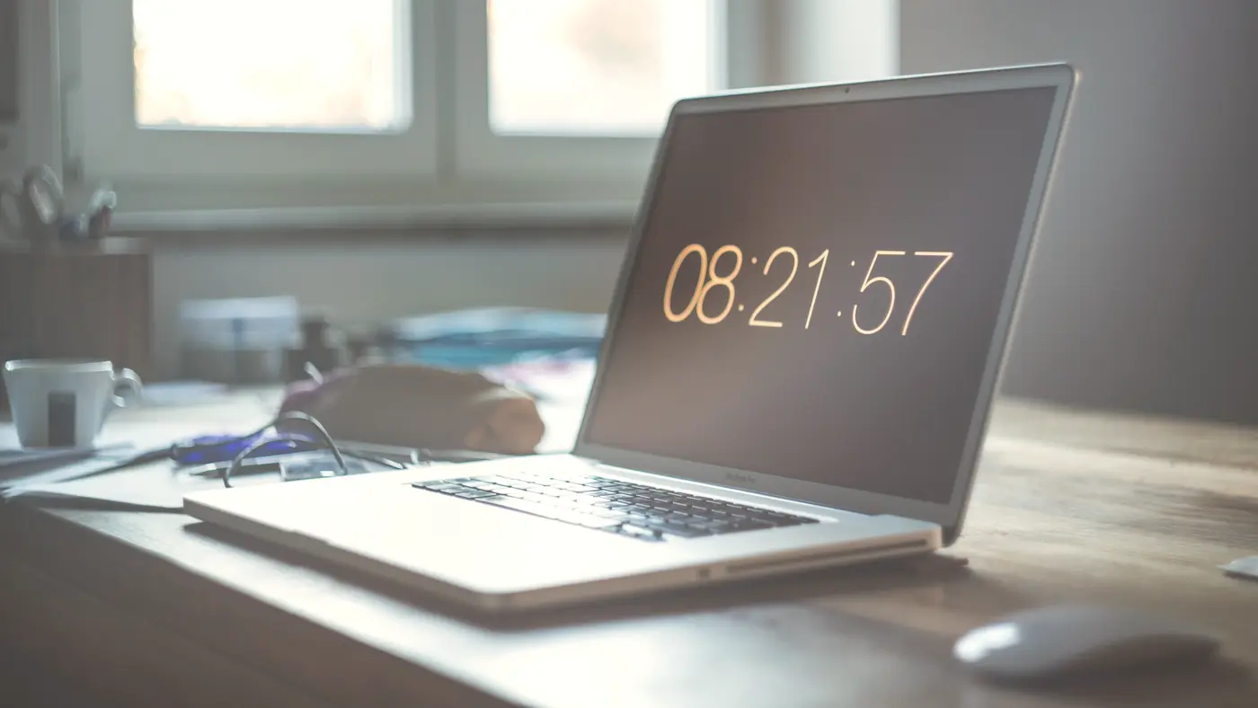 Laptop showing a digital clock on a desk by the window