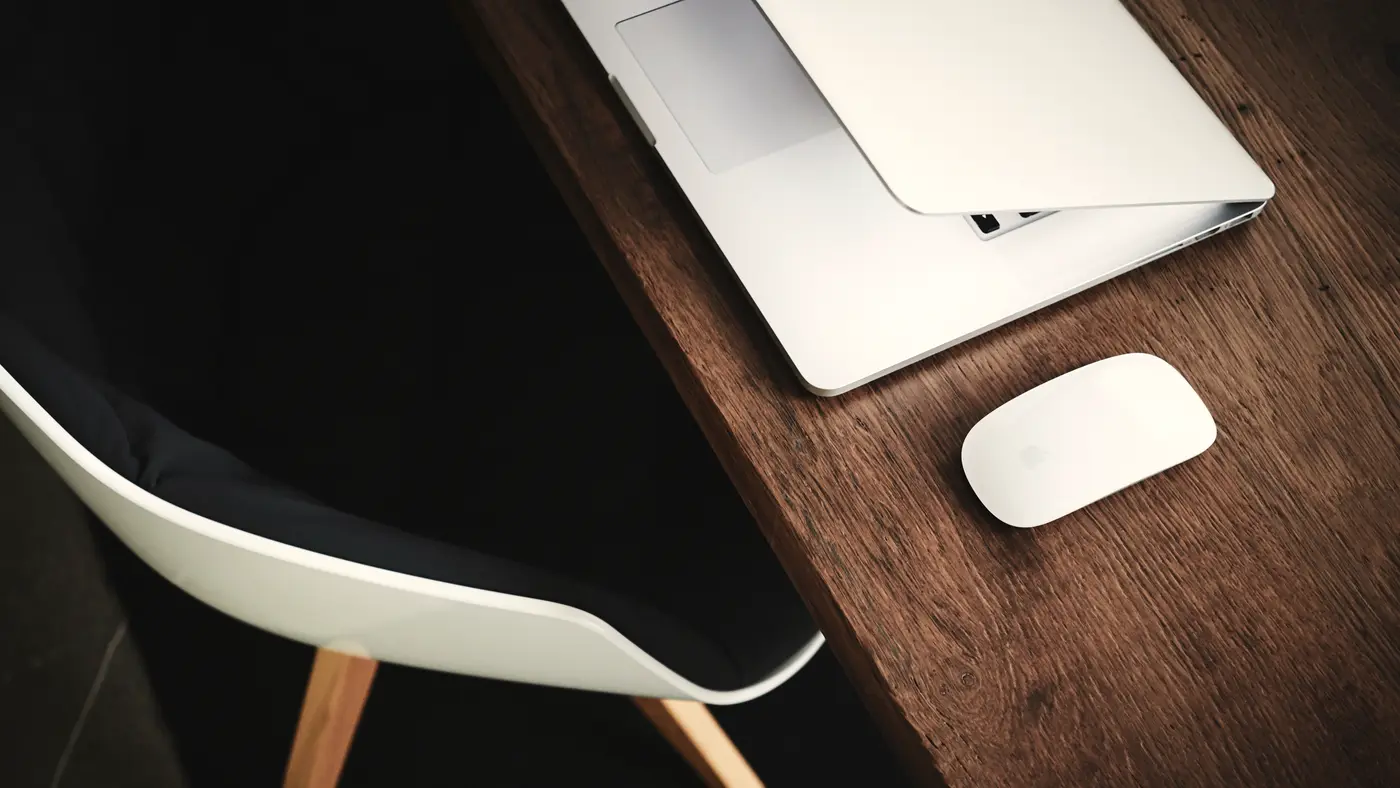 Laptop and mouse on a dark wooden desk beside a chair