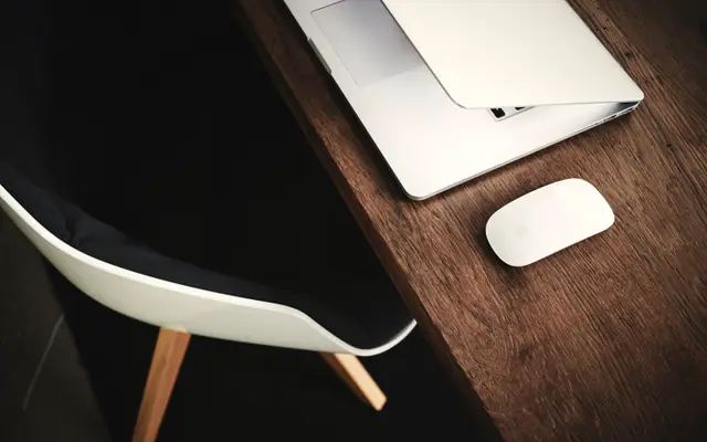 Laptop and mouse on a dark wooden desk beside a chair