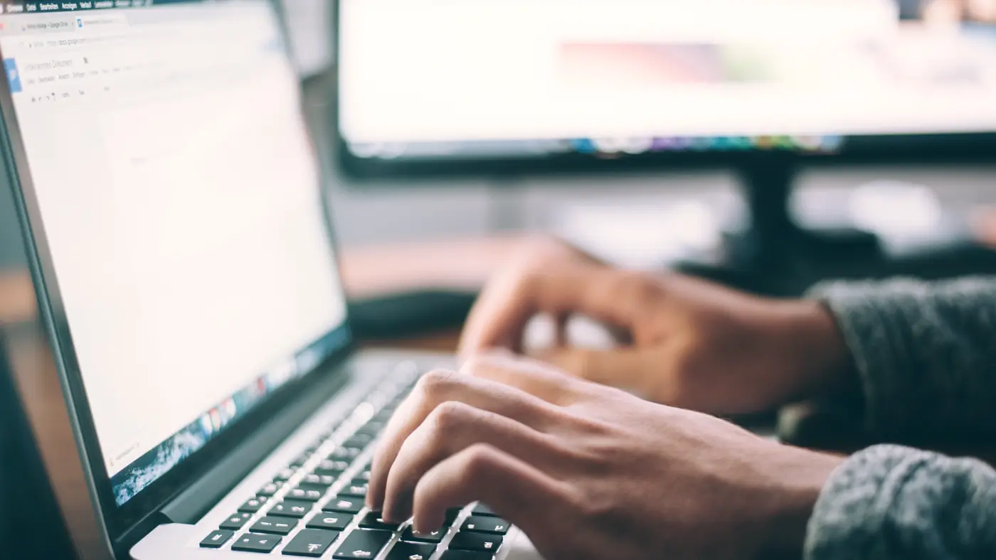 Hands typing on a laptop keyboard at an office desk