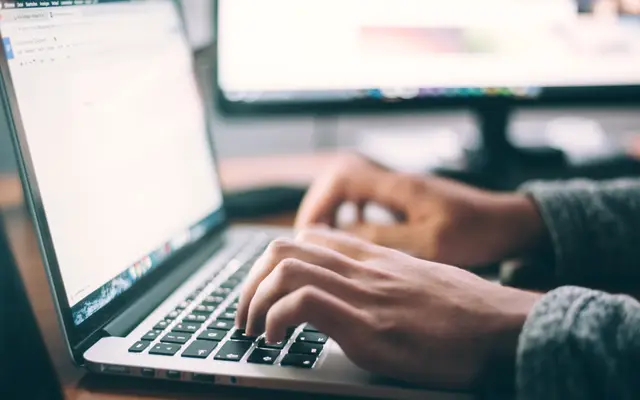 Hands typing on a laptop keyboard at an office desk