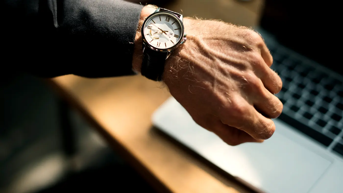 Man checking his wristwatch at a desk with a laptop
