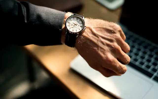 Man checking his wristwatch at a desk with a laptop