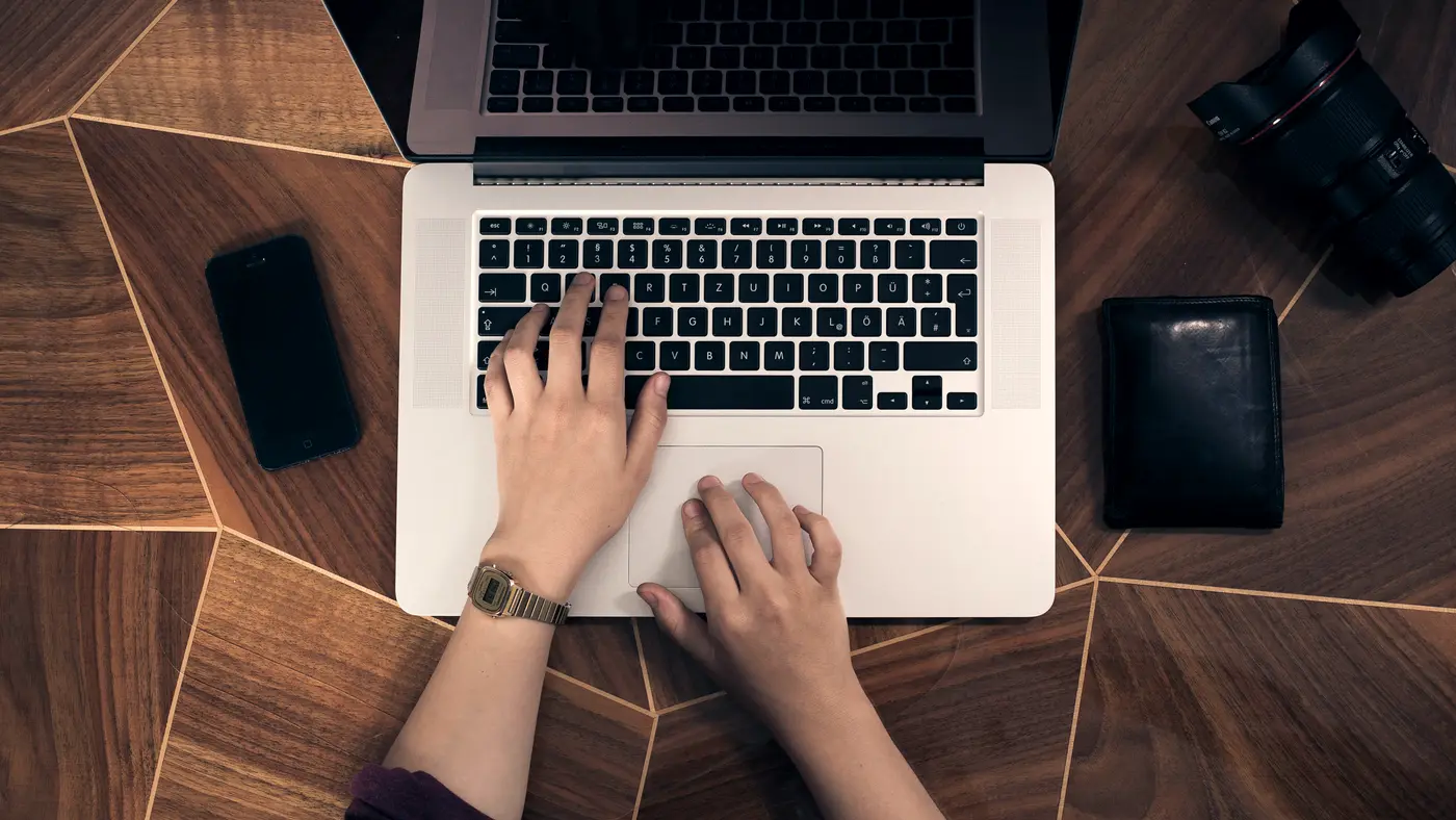 Overhead view of hands typing on a laptop on a wooden desk