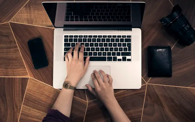 Overhead view of hands typing on a laptop on a wooden desk