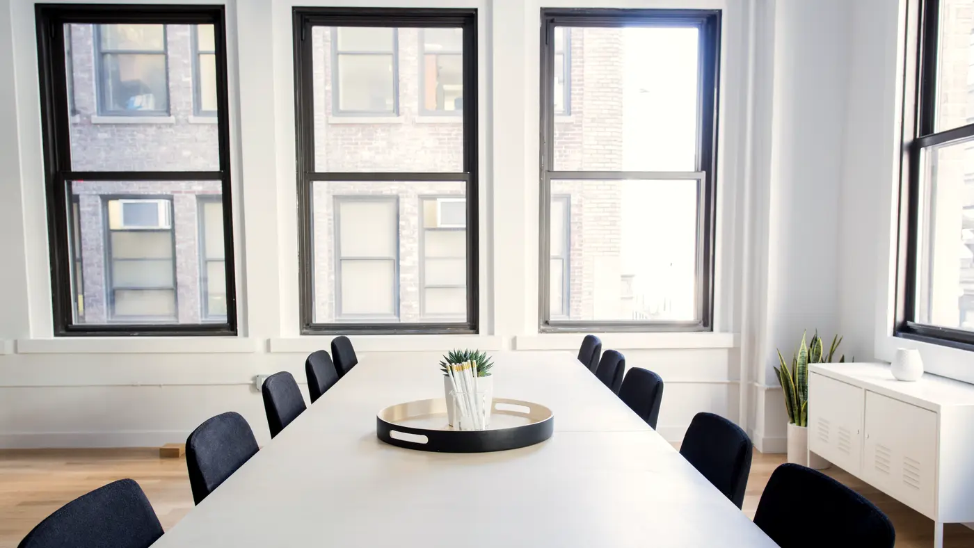 Long white meeting table with navy chairs by tall windows