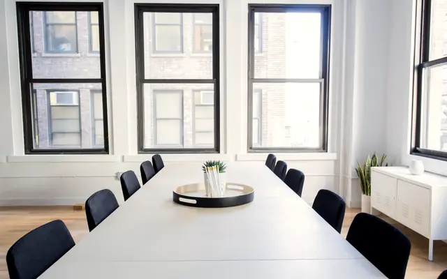 Long white meeting table with navy chairs by tall windows