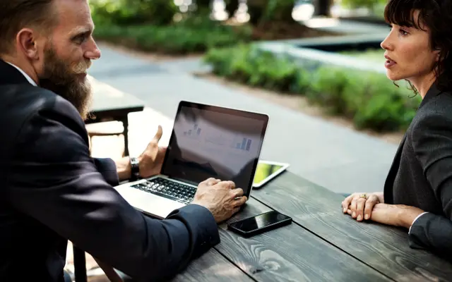 Two business people talking at an outdoor table over a laptop