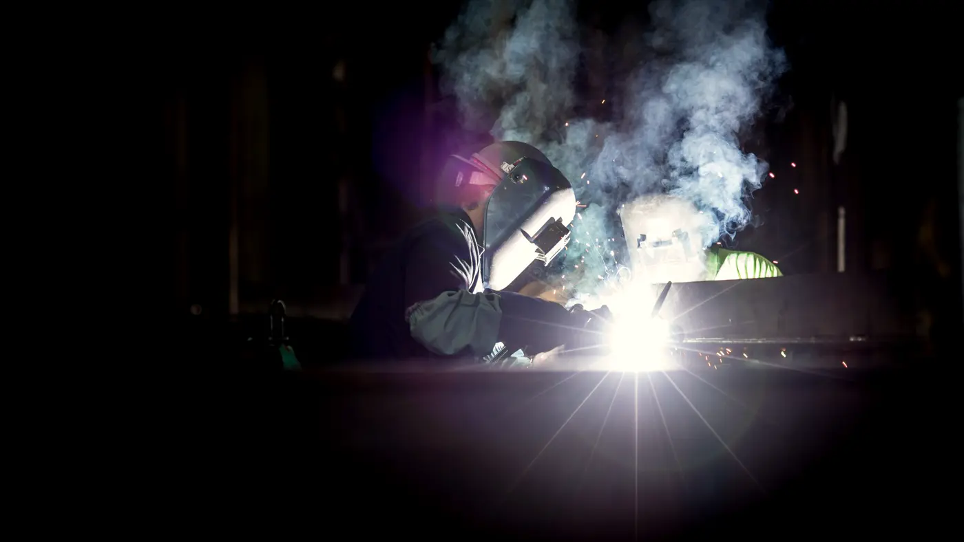 Welder in a mask working amid smoke and bright sparks