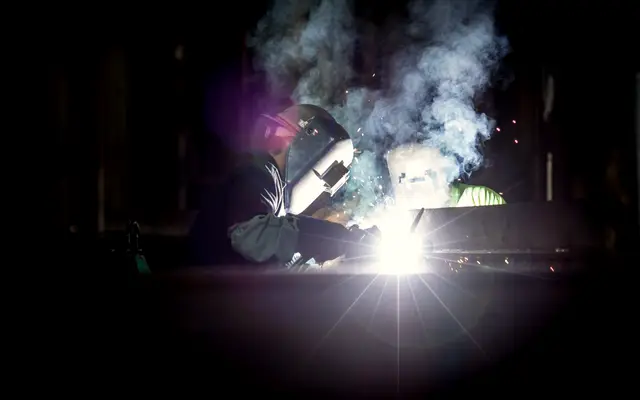 Welder in a mask working amid smoke and bright sparks