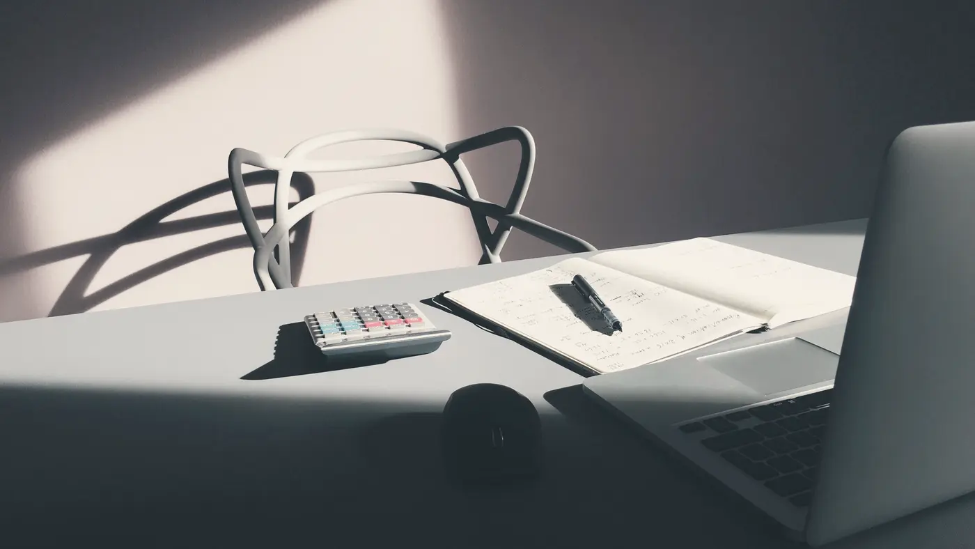 Sunlit desk with laptop, calculator and open notebook
