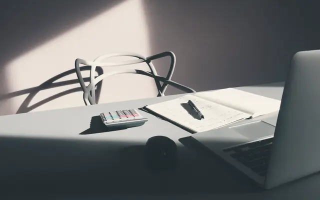 Sunlit desk with laptop, calculator and open notebook