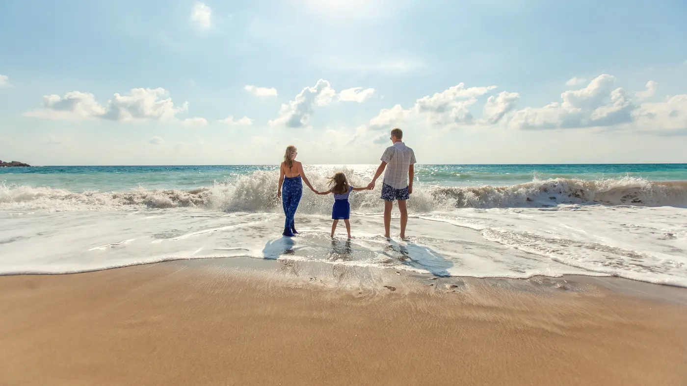 Parents and child holding hands walking into the surf on a beach