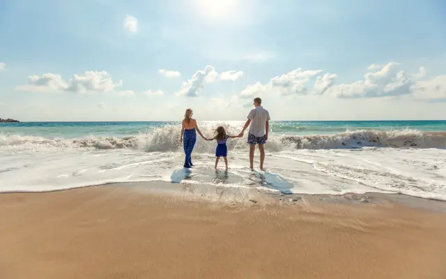 Parents and child holding hands walking into the surf on a beach