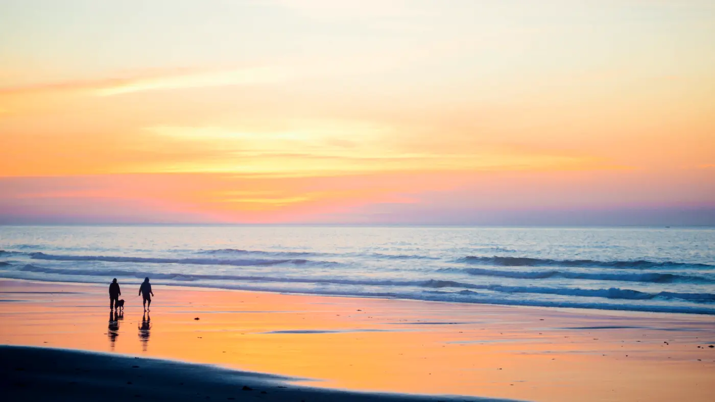 Two people walking along a quiet beach at sunset