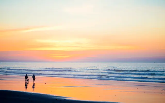 Two people walking along a quiet beach at sunset