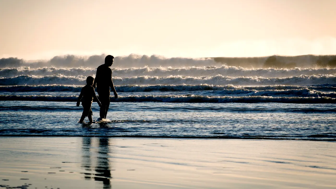 Parent and child walking through the surf at dusk