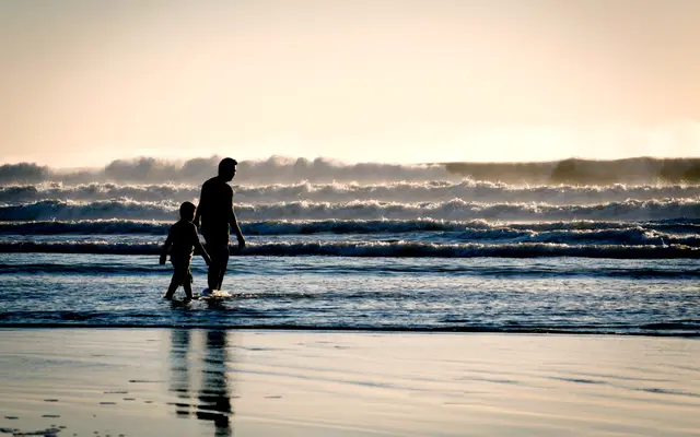 Parent and child walking through the surf at dusk