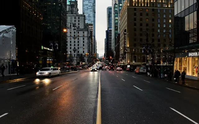 Wet downtown avenue at dusk lined with office towers