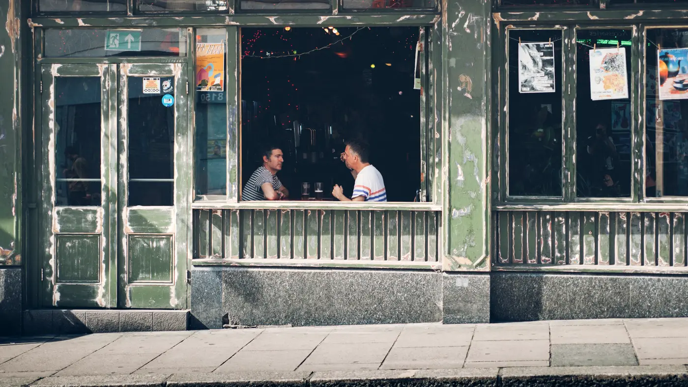 Two men chatting at the window table of a neighborhood cafe