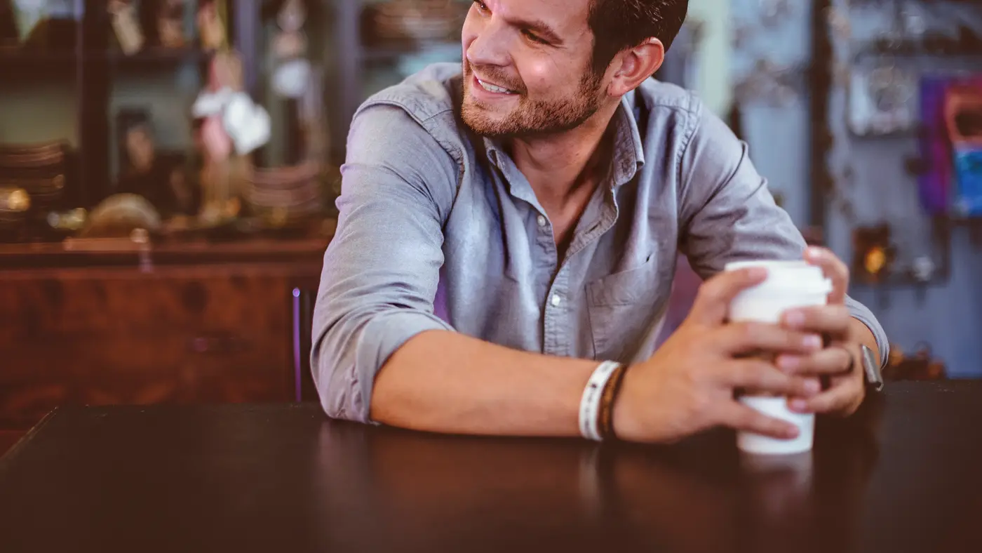 Smiling man with a coffee cup leaning on a cafe table