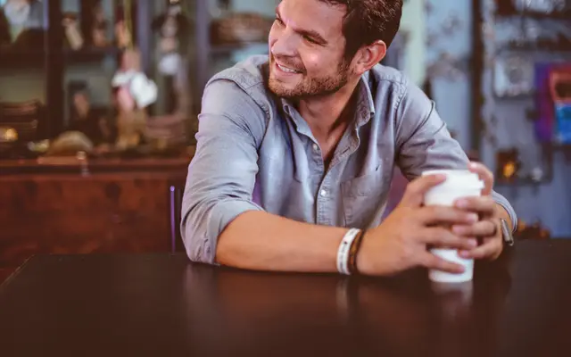 Smiling man with a coffee cup leaning on a cafe table