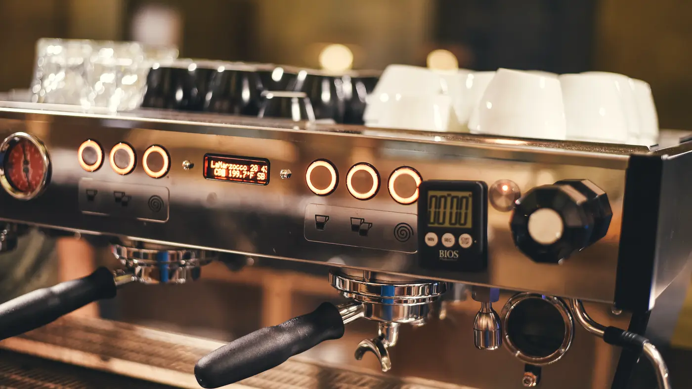 Chrome espresso machine with cups stacked on top in a cafe