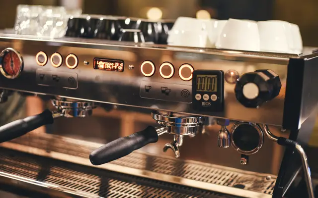 Chrome espresso machine with cups stacked on top in a cafe