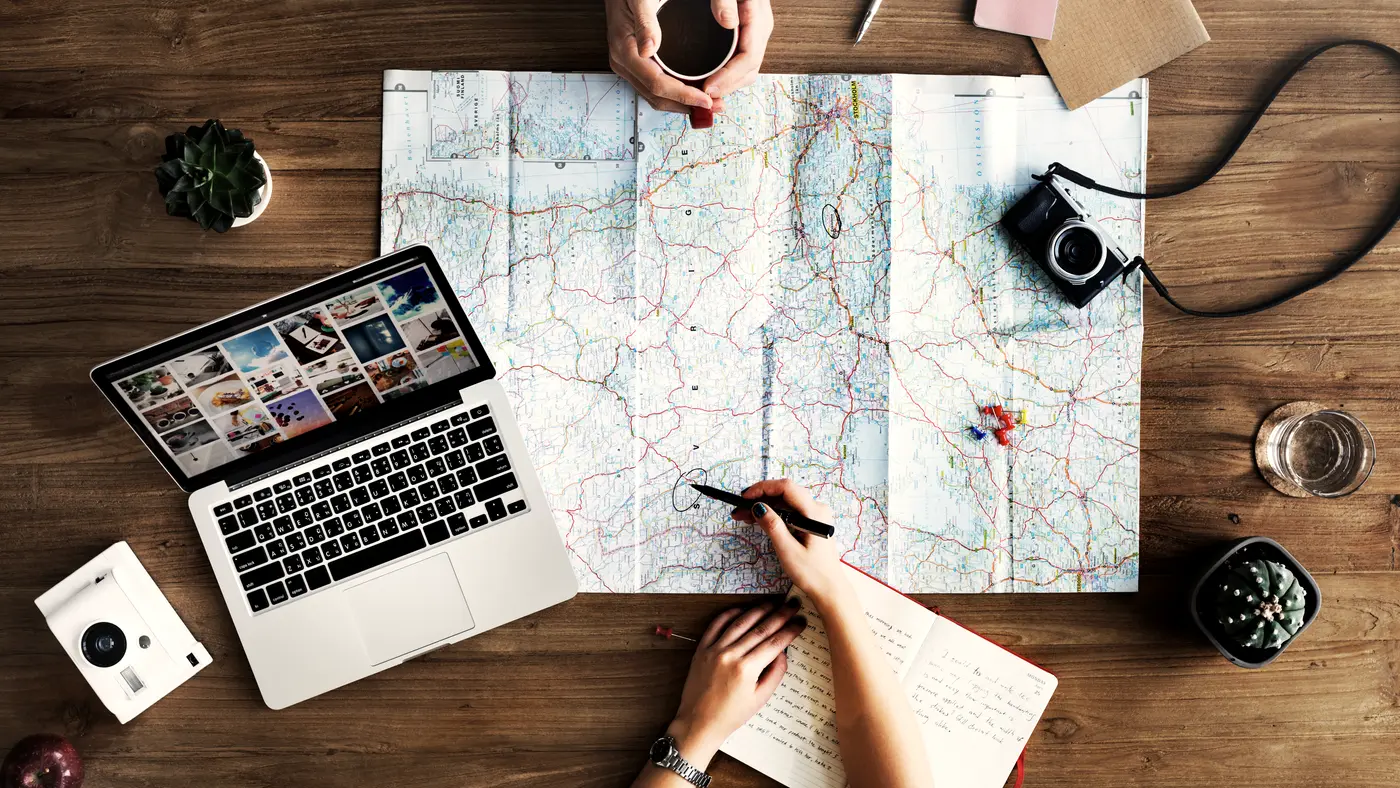 Hands marking a paper map beside a laptop on a desk
