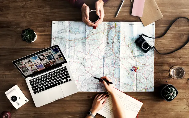 Hands marking a paper map beside a laptop on a desk