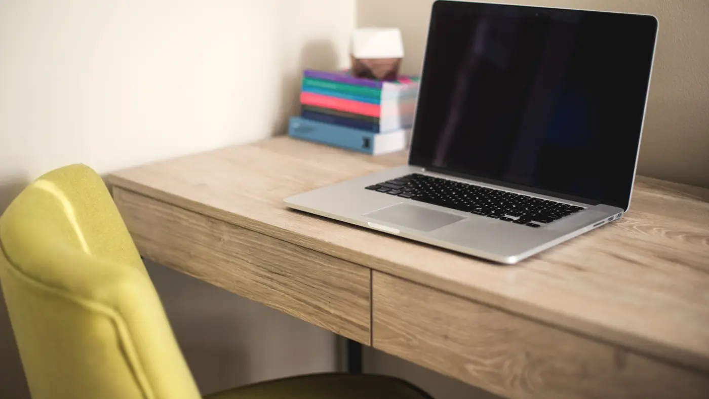 Open laptop on a light wooden desk with a yellow chair