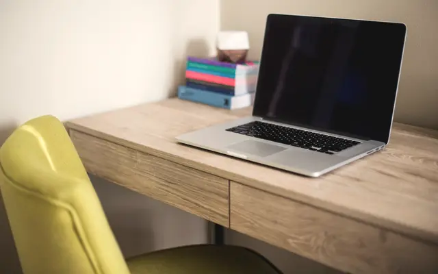 Open laptop on a light wooden desk with a yellow chair