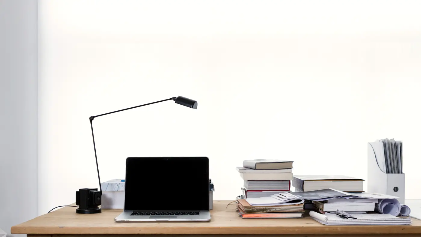 Bright minimal desk with laptop, lamp and stacked books