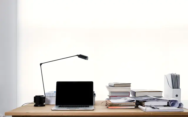 Bright minimal desk with laptop, lamp and stacked books
