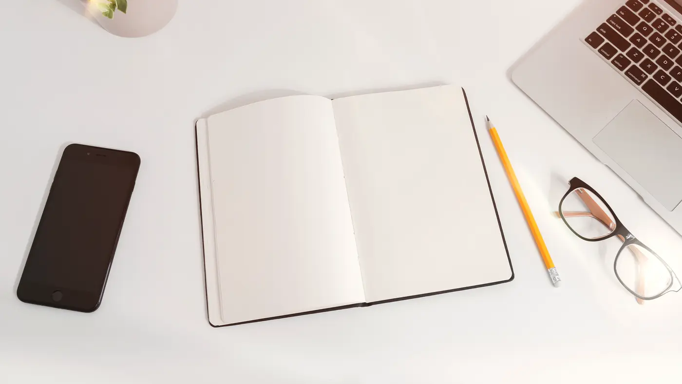 Blank open notebook with pencil, glasses and phone on a desk