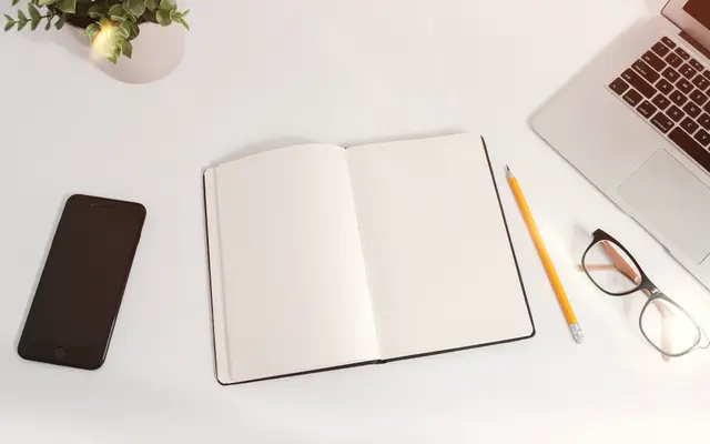 Blank open notebook with pencil, glasses and phone on a desk