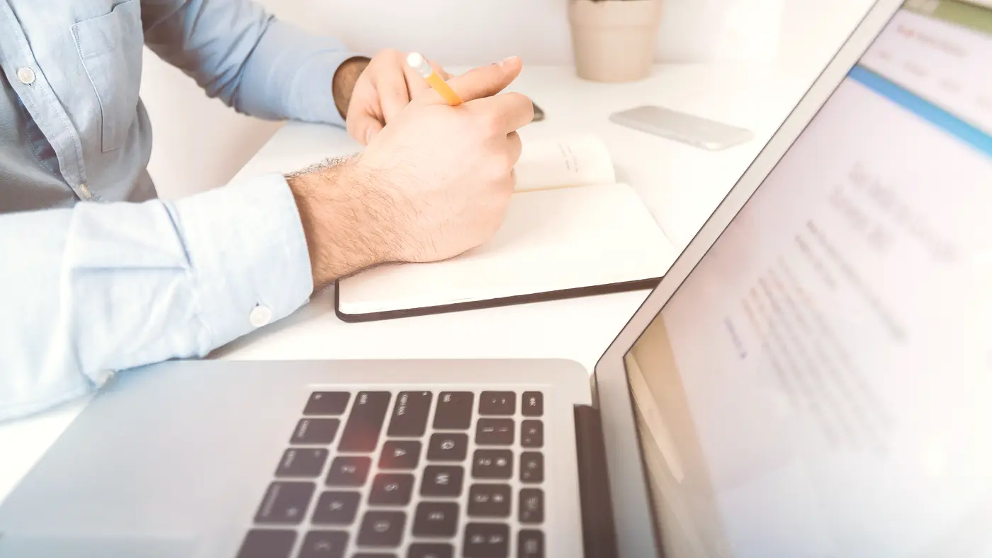 Man making notes beside a laptop at a white desk