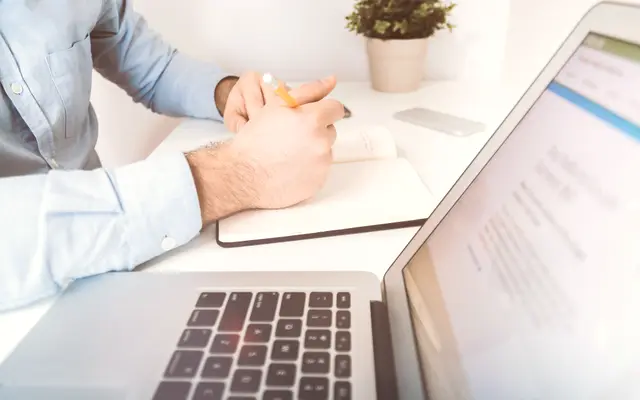 Man making notes beside a laptop at a white desk