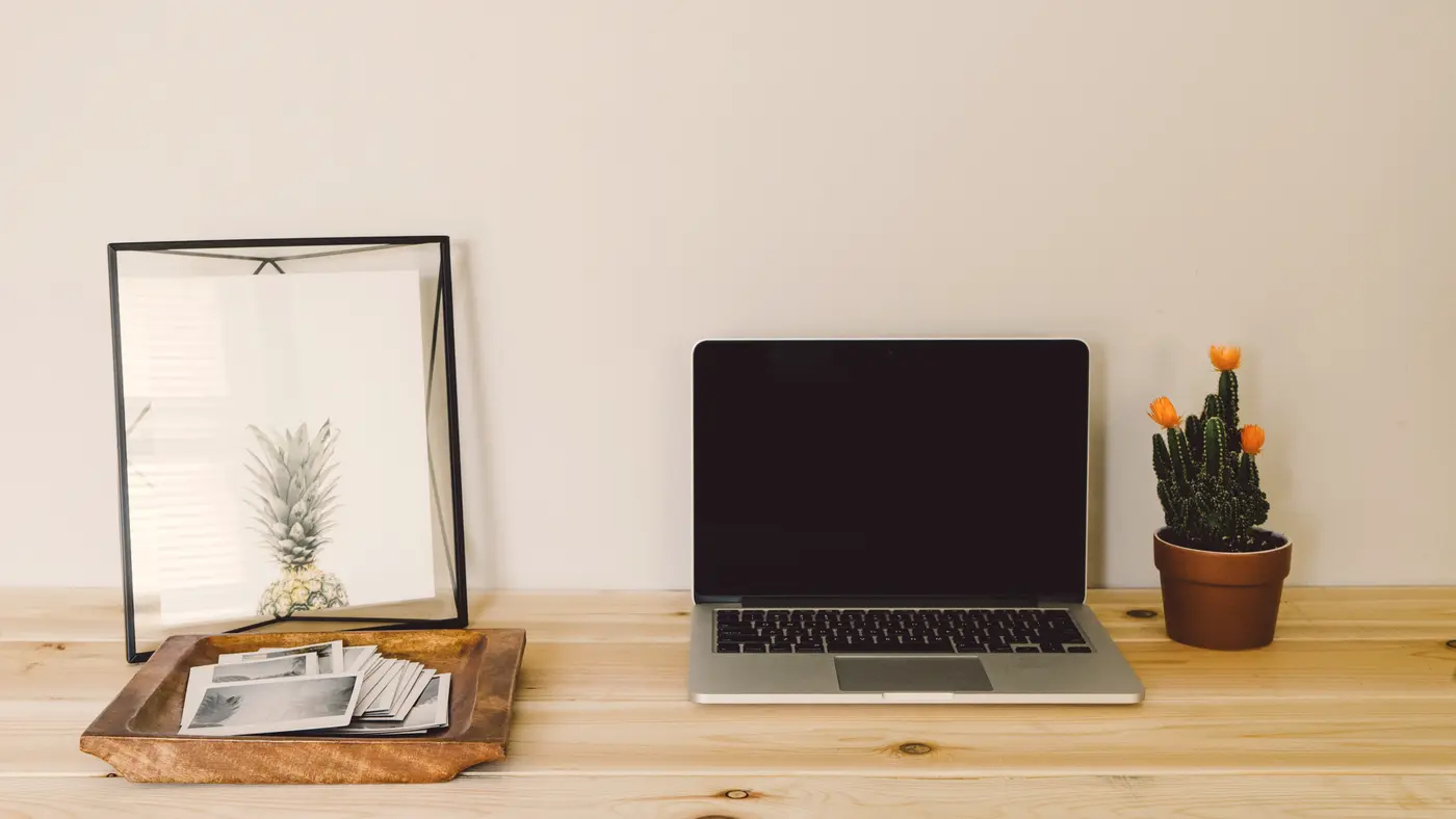 Laptop on a wooden desk with a small cactus and picture frame